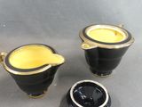 two black and gold teapots and a saucer on a table