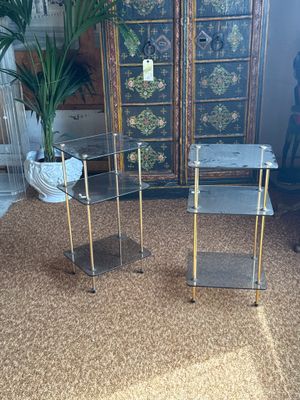 pair of glass and brass side tables in a room with a potted plant in the corner