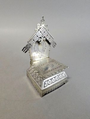 une petite horloge en argent posée sur un socle, sur une table