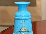 a blue vase sitting on a glass table with a picture in the background