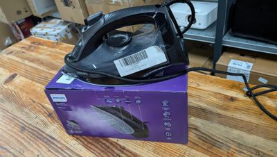 un fer à repasser à vapeur noir et argent posé sur une boîte violette