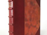 an old book with a red cover sitting on top of a white table