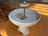 a white fountain sitting on the ground next to a wooden bench