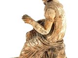 an old statue of a woman sitting on a rock reading a book