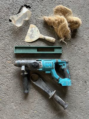 une perceuse filaire, un marteau et un pinceau posés par terre