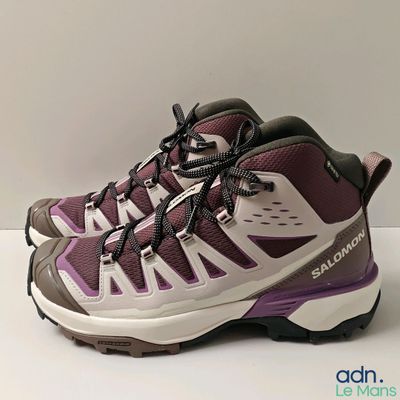 des chaussures de randonnée violettes et blanches à lacets, posées sur une surface blanche