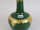un vase vert orné de motifs dorés sur un fond blanc