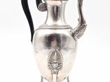 une théière ancienne en argent, dotée d'une anse noire et posée sur un socle