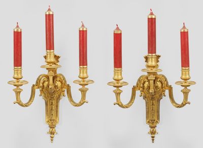 three red candles are lit on a gold wall sconce