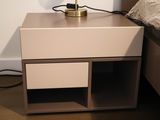 a nightstand with a lamp on top of it next to a bed