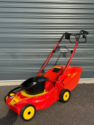 une tondeuse à gazon rouge aux roues jaunes garée devant un garage