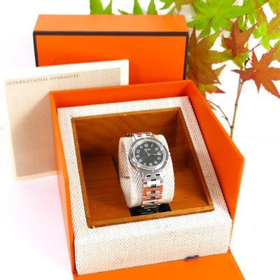 an orange box with a watch inside of it and a plant in the background