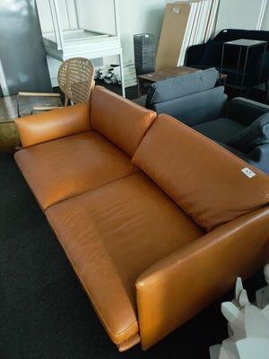 a brown leather couch sitting in a room with other furniture in the background