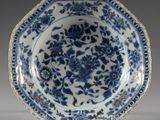 assiette bleue et blanche ornée de fleurs et de feuilles, posée sur un socle