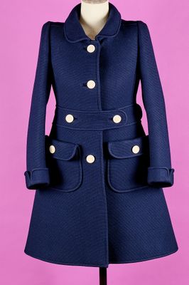 un manteau bleu posé sur un mannequin, devant un fond rose