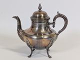 an antique silver teapot with a bird handle on a stand