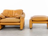 two brown leather chairs and a foot stool in a white room