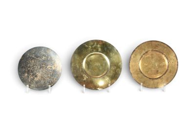 Trois assiettes sont alignées sur une surface blanche : l'une est dorée et l'autre est argentée.