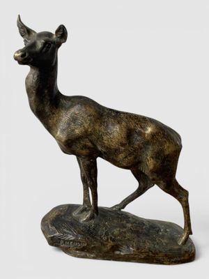 statue en bronze représentant un cerf debout sur un rocher, sur fond blanc