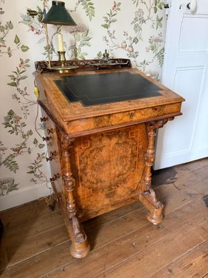 un bureau en bois avec un plateau noir dans une pièce au papier peint à motifs floraux