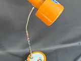 une lampe de bureau orange, avec son cordon, posée sur une surface grise