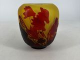 yellow and red glass vase with red flowers on it on a white surface