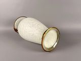 a white vase with a gold rim sitting on a gray surface