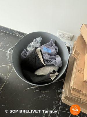 a bucket full of clothes sitting on the floor next to a pile of boxes