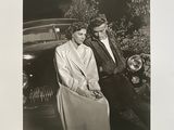 photographie en noir et blanc d'un homme et d'une femme debout à côté d'une voiture