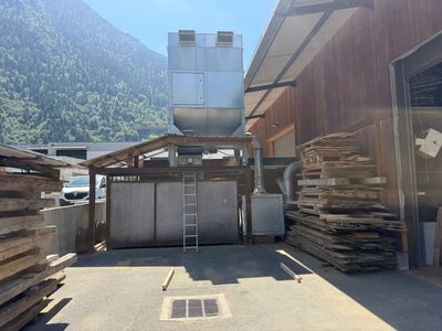 Plusieurs piles de bois sont empilées devant un bâtiment, avec une montagne en arrière-plan.