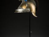 un casque posé sur un support, orné d'une plume rouge, blanche et bleue