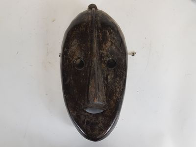 an old wooden mask hanging on a wall on a white wall