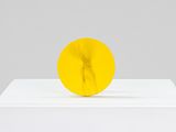 une sculpture jaune posée sur un socle blanc