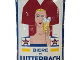 une vieille enseigne en tôle faisant la promotion d'une bière et représentant une femme tenant un verre de bière
