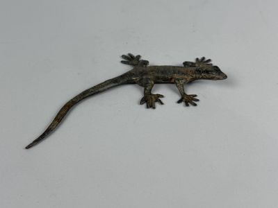 small metal geckole sitting on a white surface with a white background