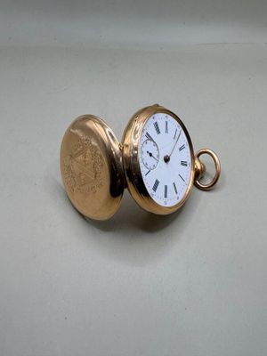 une montre de poche en or avec un cadran blanc sur une surface blanche