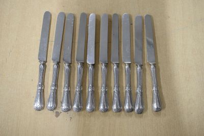 six couteaux en métal argenté sont alignés sur une table en bois