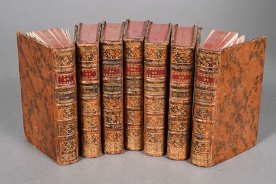 six old books lined up in a row on a gray surface