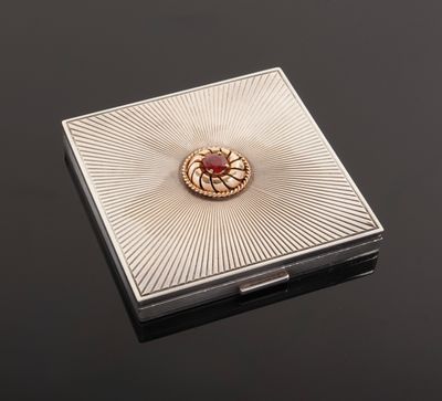 a close up of a silver box with a red stone in it