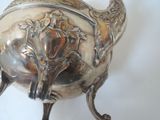 a silver tea pot with a handle on a stand