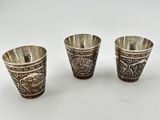 three silver cups with designs on them on a white surface