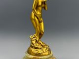 une statue en or représentant un homme coiffé d'un chapeau, posée sur un socle en marbre