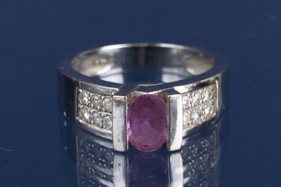 une photo d'une bague sertie d'un rubis et de diamants posée sur une surface réfléchissante