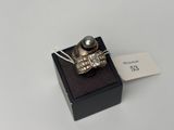 une bague en argent ornée d'une perle noire, posée sur un écrin noir