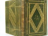 an old book with gold and green cover sitting on a white surface