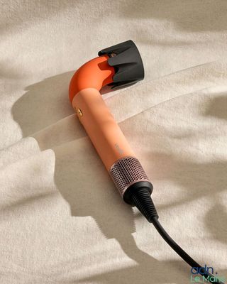 un sèche-cheveux orange posé sur un lit, muni d'un cordon noir