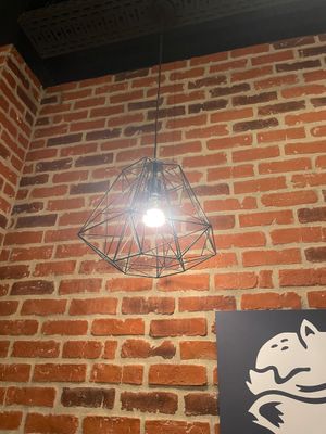 une lampe suspendue au plafond au-dessus d'une enseigne fixée sur un mur de briques