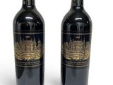 two bottles of red wine sitting next to each other on a white surface