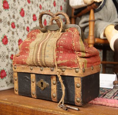 une petite valise posée sur une table, avec une poupée en arrière-plan