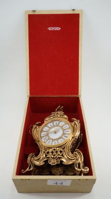 une horloge dorée dans un coffret rouge posé sur une surface blanche